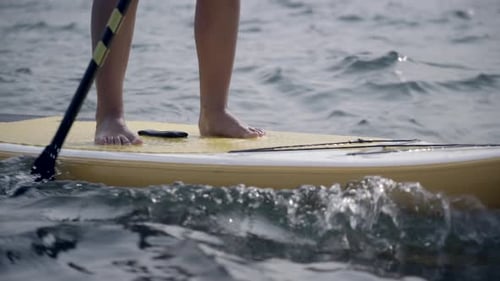 Close-up view of feet on paddleboard as it passes, slow motion