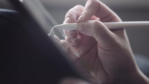 Close up of a hand holding a pen and drawing on a tablet