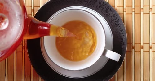 Tee aus einer Glasteekanne in eine Tasse auf dem Küchentisch gießen