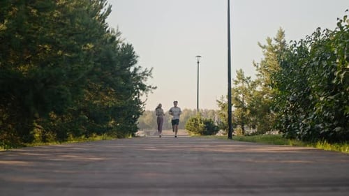 Route entre les arbres et couple actif en bonne santé faisant du jogging vers la caméra