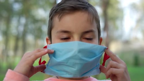 Child Putting On a Blue Face Mask Outdoors