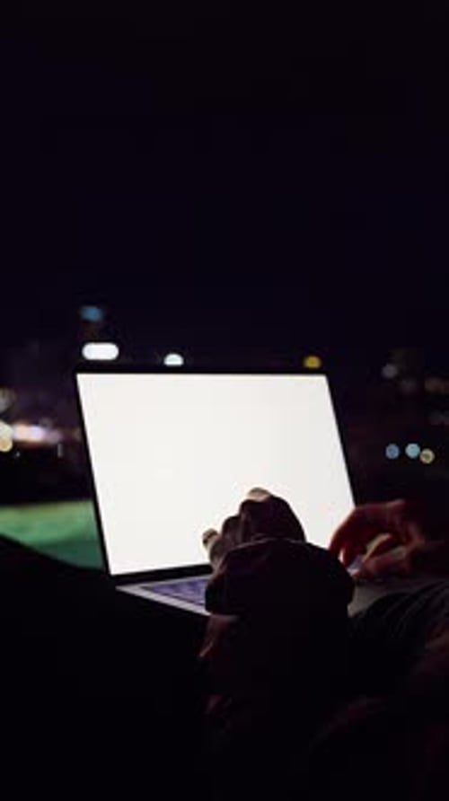 Vidéo verticale. Femme travaillant sur un ordinateur portable avec une maquette d'écran blanc brillant contre la ligne d'horizon nocturne de la ville