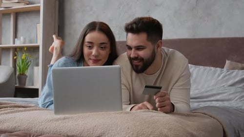 Caucasian Happy Couple Woman and Man Relax on Bed with Laptop Shopping Online Use Bank Credit Card