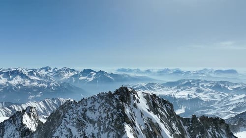 Drone shot of a climber standing on a rocky peak in the Alps.