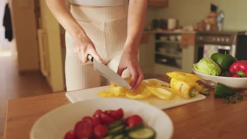 Close-up of young woman's hands cutting peppers making salad at home in the kitchen