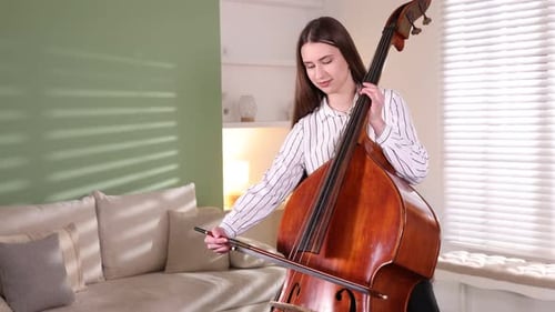 Woman Practices Cello in Living Room During the Day