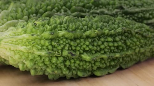 Une gourde amère, un légume souvent utilisé comme ingrédient en cuisine, est posée sur une table en bois.