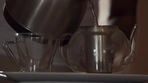Brewing tea: Hot water from kettle poured into glass teapot, close up