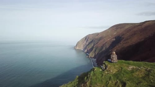 Aerial Panning Drone Shot of Woman Sat on Cliff Overlooking Coastal View