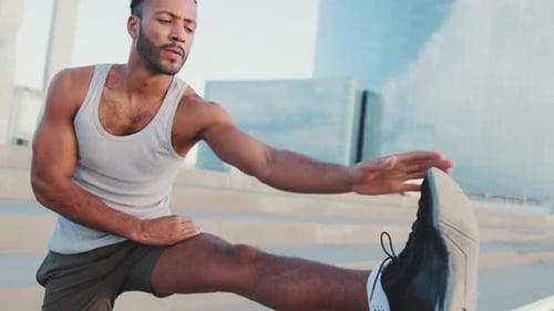 Young athlete doing warm-up, stretching legs before training while standing on the embankment
