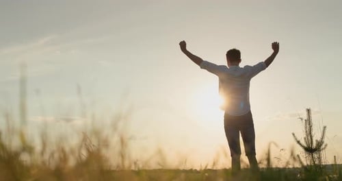 A Young Energetic Man Raises His Hands Up Stands at Sunset in a Picturesque Place Success and