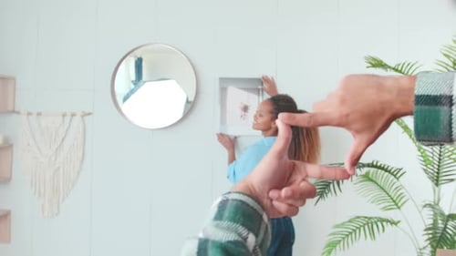 Woman Hanging Picture Framed by Hands Indoors