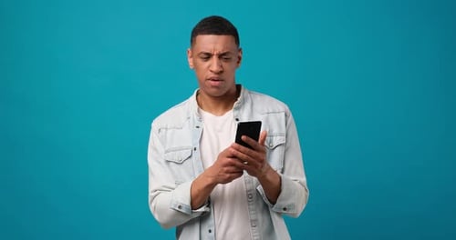 Young African American Man Using Mobile Cell Phone Typing When Looking at Camera Surprised and