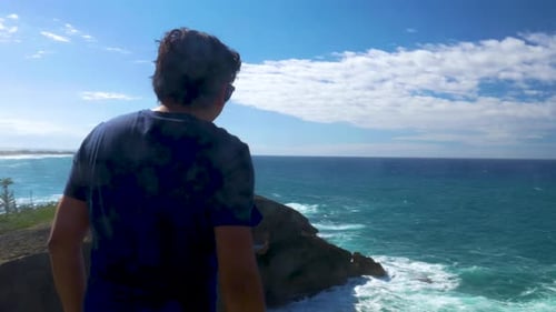 Man walking towards a cliff facing the sea while lifting his hands on celebration.