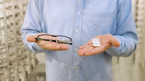 Hombre mayor sostiene lentes de contacto y anteojos en las manos de cerca
