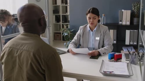 Woman Provides Stamped Documents Across Desk to Man