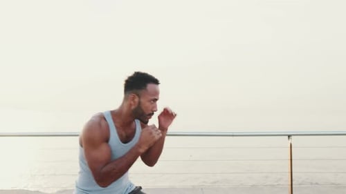 Young fit athlete boxer practicing punching technique while standing on the embankment