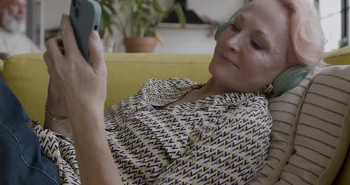 Senior Adult Woman Wearing Headphones Listening to Music on Sofa at Home