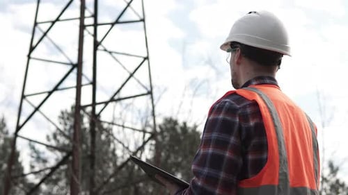 Engineer Inspecting Electrical Tower with Tablet