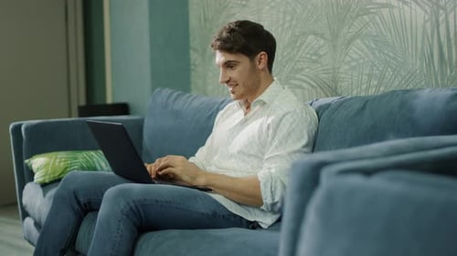 Excited man working on laptop sitting on couch
