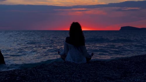 Silhouette of woman concentrated on yoga pose exercising on the beach during colorful sunset