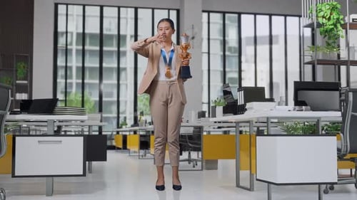 Femme d'affaires avec médaille d'or et trophée montrant les pouces vers le bas pour ridiculiser le perdant au bureau