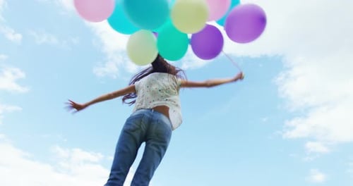 Young Woman Jumping with Balloons Against Blue Sky