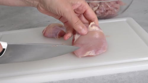 O chef corta carne de frango crua em uma tábua branca