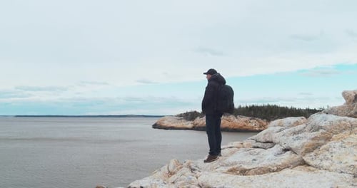 Man Standing with a Backpack on a Rocky Mountain and Looking at the Ocean