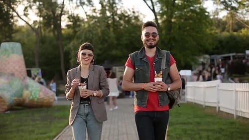 Casal hippie estiloso caminhando comendo sorvete e waffles rindo no parque da cidade, jovem romântico