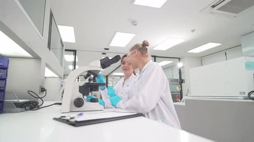Two Young Women Working with Microscope in Lab