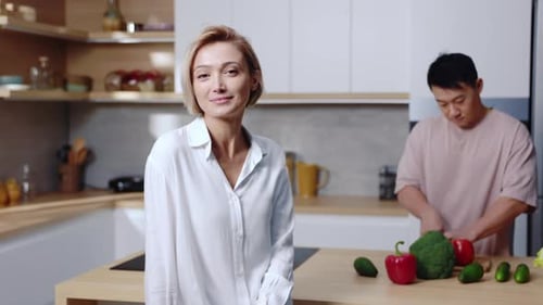 Woman smiles, man prepares vegetables in modern kitchen
