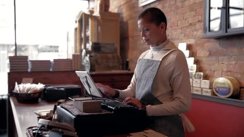 Female Shop Owner Using Digital Tablet Cash Register At Counter