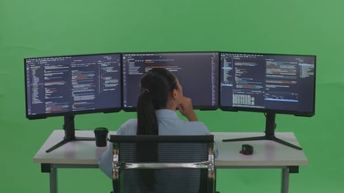 Back View Of Woman Thinking About Something While Write Code With Multiple Screens In Green Screen