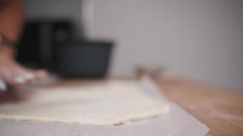 A woman, using a wooden rolling pin, rolls out the dough and touches it with her hands in slow mo