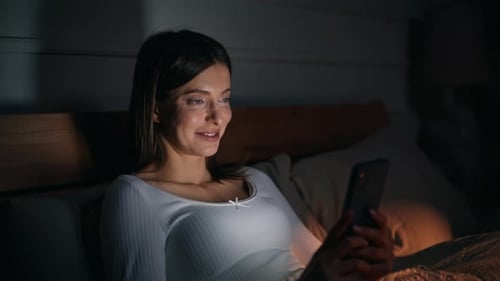Smiling Woman Using Smartphone in Bed at Night