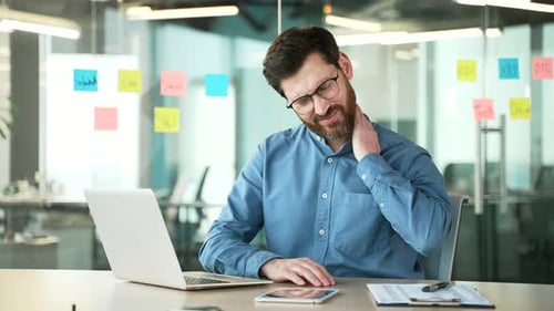 Bearded Man Massaging Neck in Office