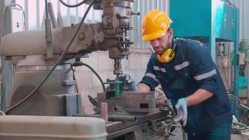 Junger kaukasischer Ingenieur, der eine Drehmaschine bedient, um die Produktion in einer industriellen Fabrik vorzubereiten.