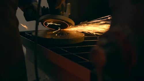 Close-up shot of a worker using an angle grinder to cut or polish metal, creating a dramatic shower