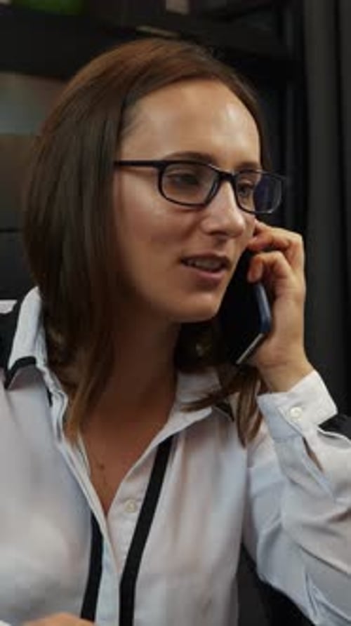 Young smiling female is talking on phone in modern office. Vertical video