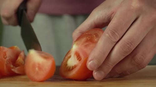 Hands of middle man european slices a tomato with kitchen knife on cutting board, front side view