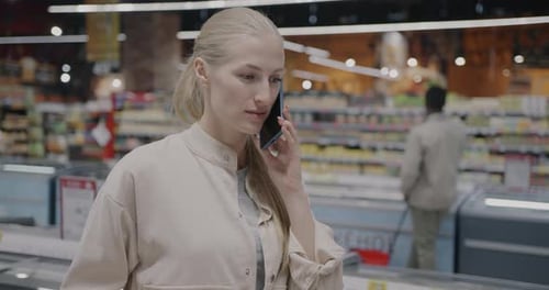 Beautiful Young Lady Speaking on Mobile Phone Walking in Supermarket Shopping in Retail Store