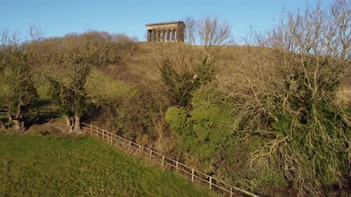 Vue inclinée vers le haut d'une ancienne structure de piliers visible à une distance derrière des champs agricoles accrochés à un arbre