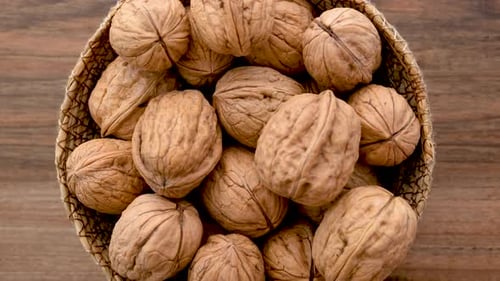 Close Up View Of A Wicker Bowl Filled With Shelled Walnuts Rotates On A Wooden Surface