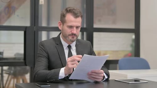 Adult Reviews Paperwork With Pen in Office