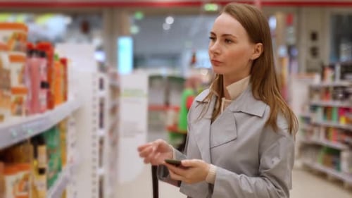Focused Woman Using a Smartphone in a Grocery Store A Young Woman Reads a Checklist Using Her