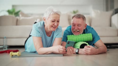 Senior Couple Relaxing With Phone After Home Workout