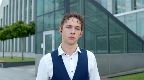 Junger Mann mit Ohrhörern vor einem modernen Gebäude in lässiger Weste