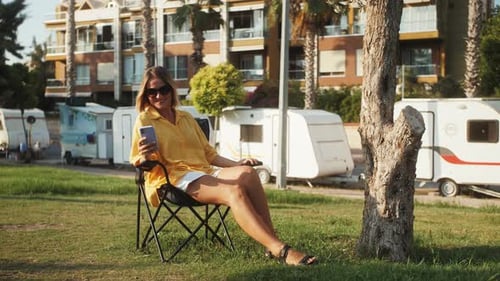 Woman Relaxing with Phone Near Trailers on Sunny Day