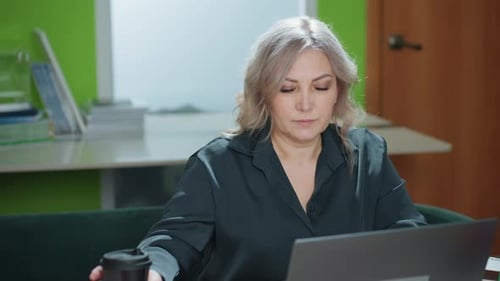 Woman working at laptop while drinking coffee